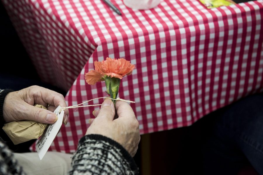 A table with a red and white checked table clothe on. A pair of hands hold on to a flower with a tag attached.