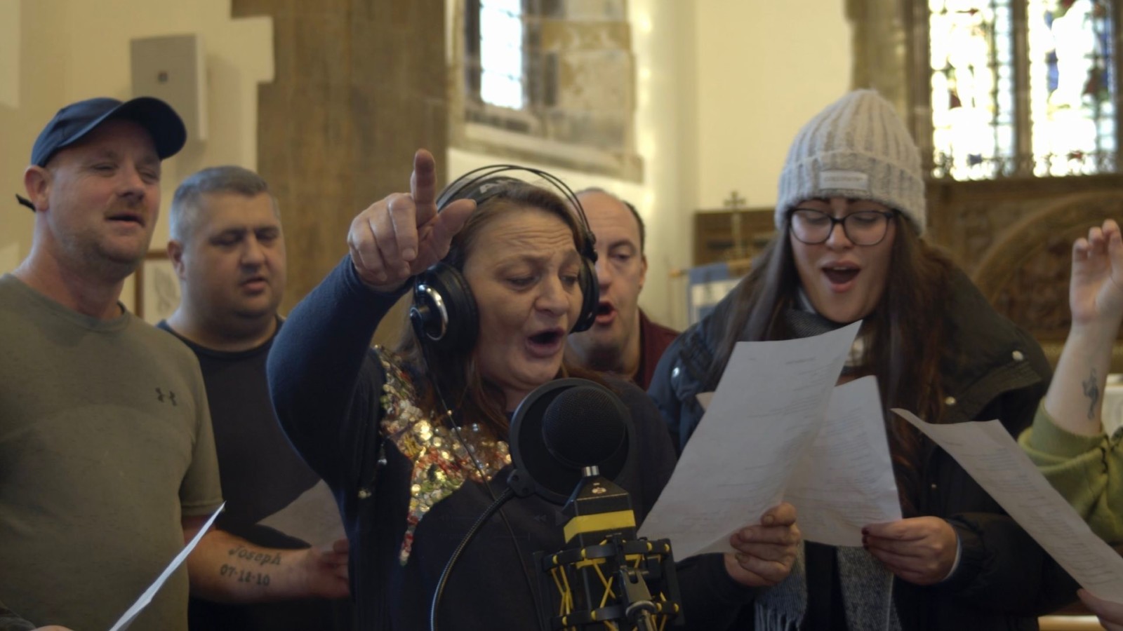 A group of people stand in front of a microphone singing and smiling.