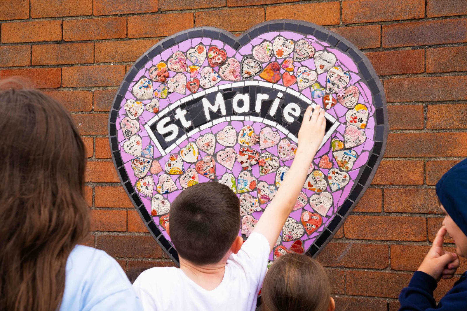 A child with short brunette hair wearing a white t shirt reaches up to the mural with one hand.