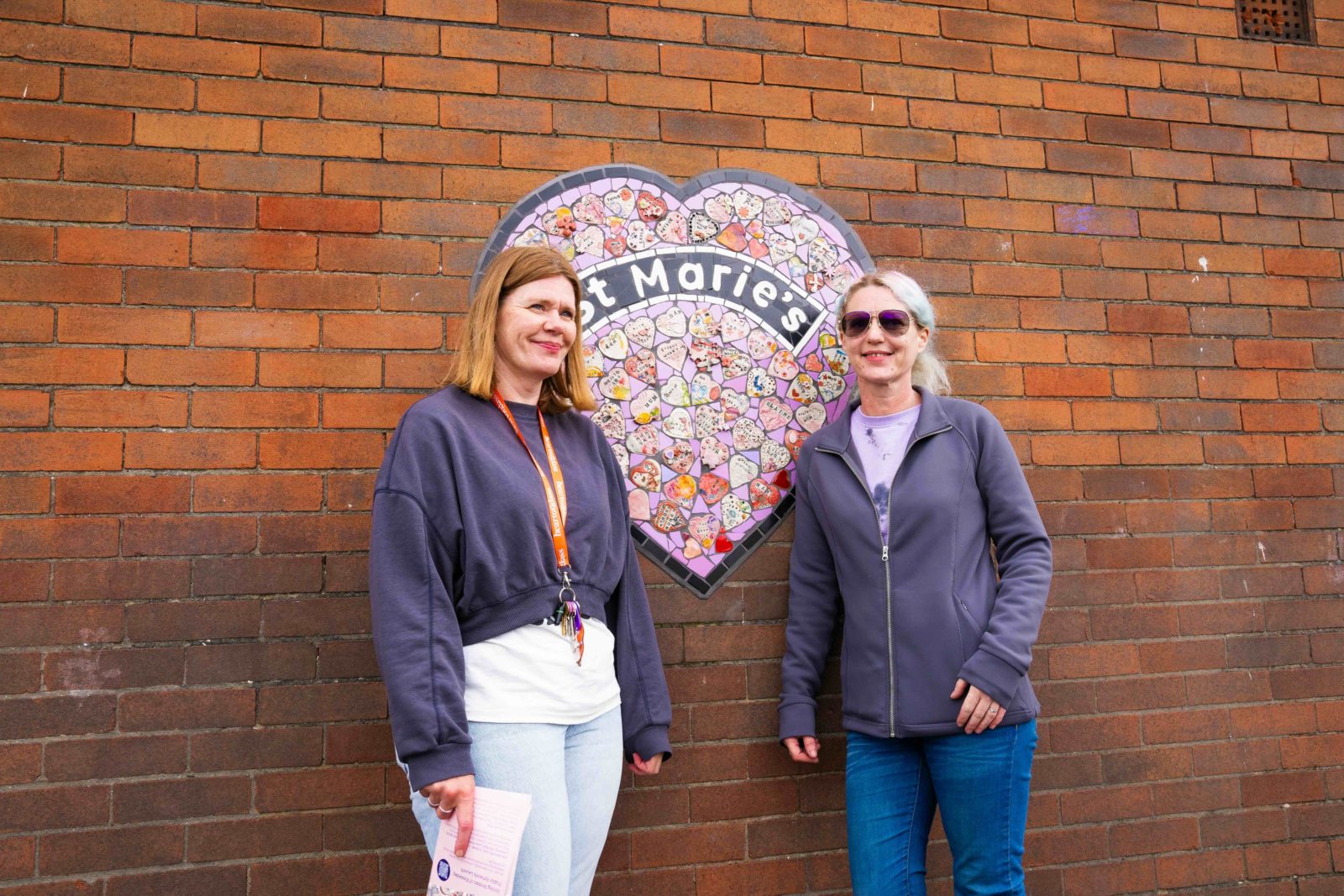 Heart of Glass producer Anna smiles standing in front of the mosaic next to artist Claire.