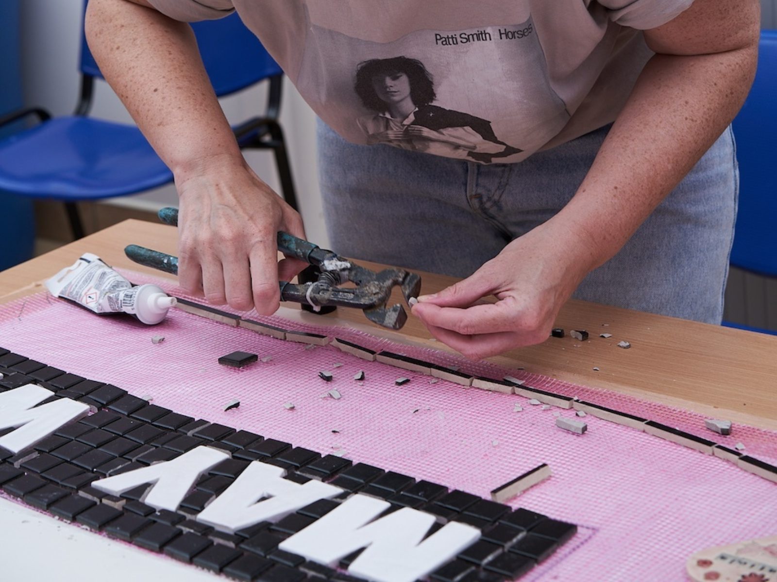 A woman uses tools to cut and place mosaic tiles