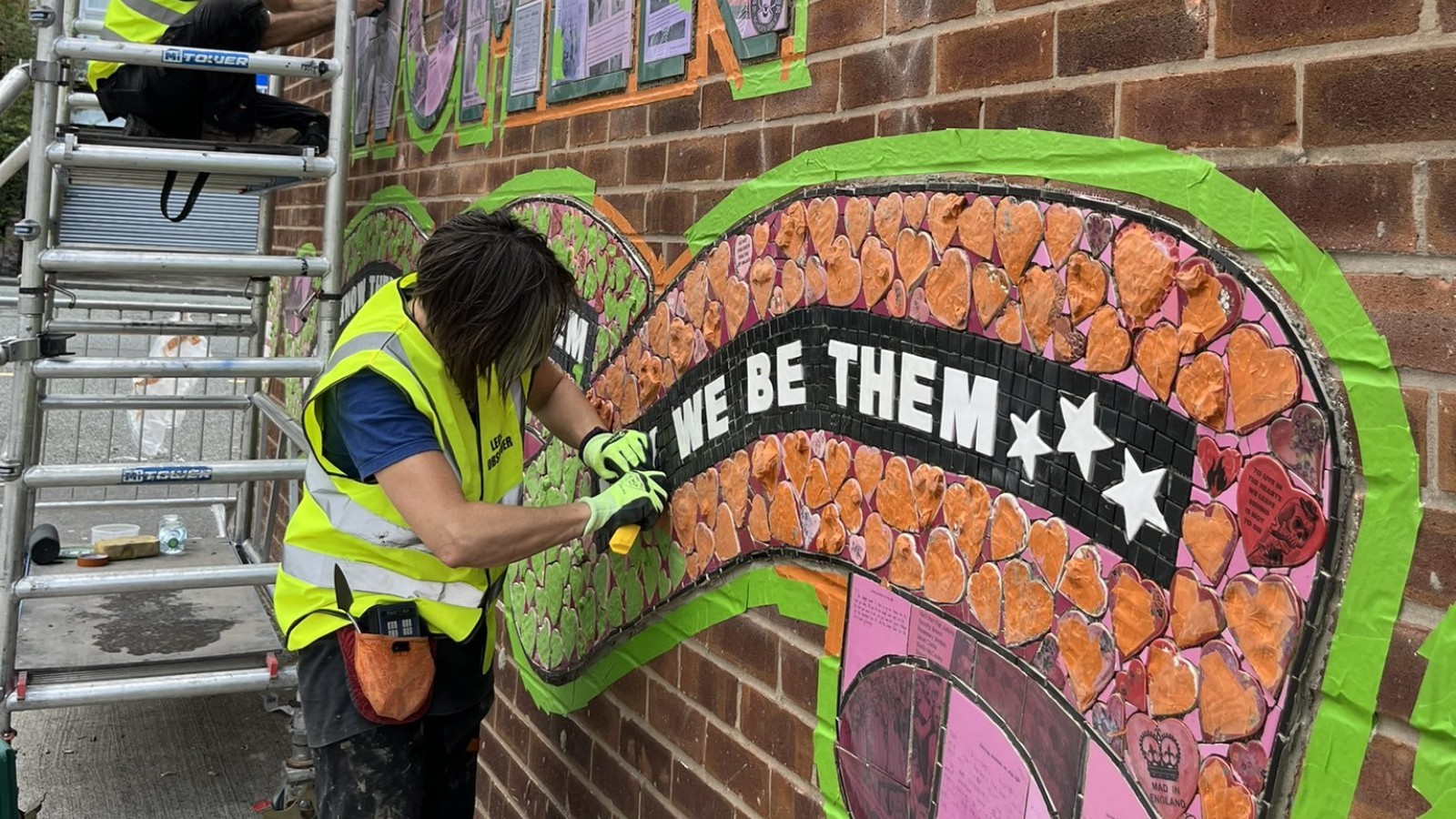 A person wearing a hi vis vest installing a mosaic mural onto a brick wall