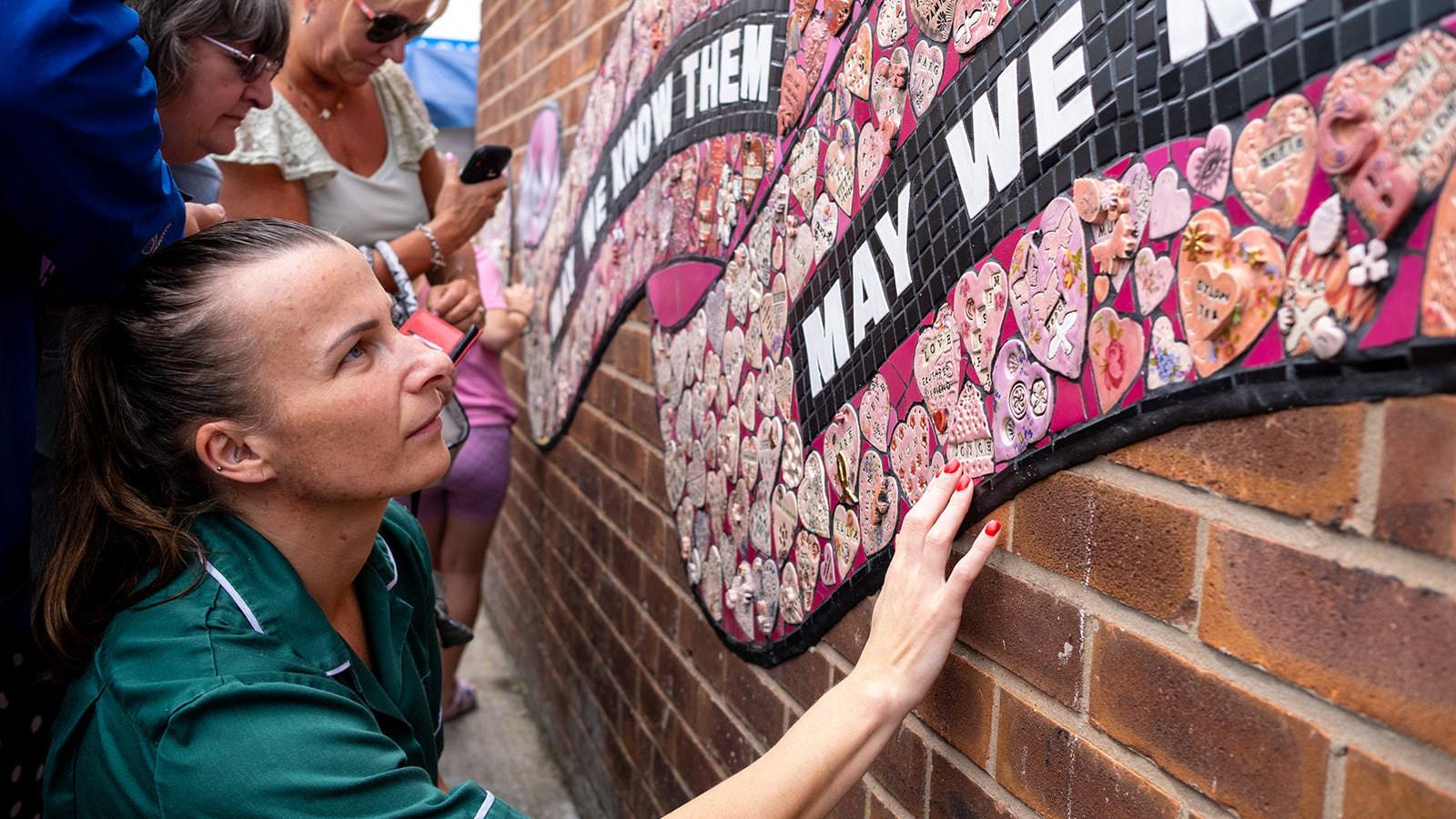 A woman in a nurse's uniform looks up close at the mosaic with one hand on it, her expression is thoughtful.