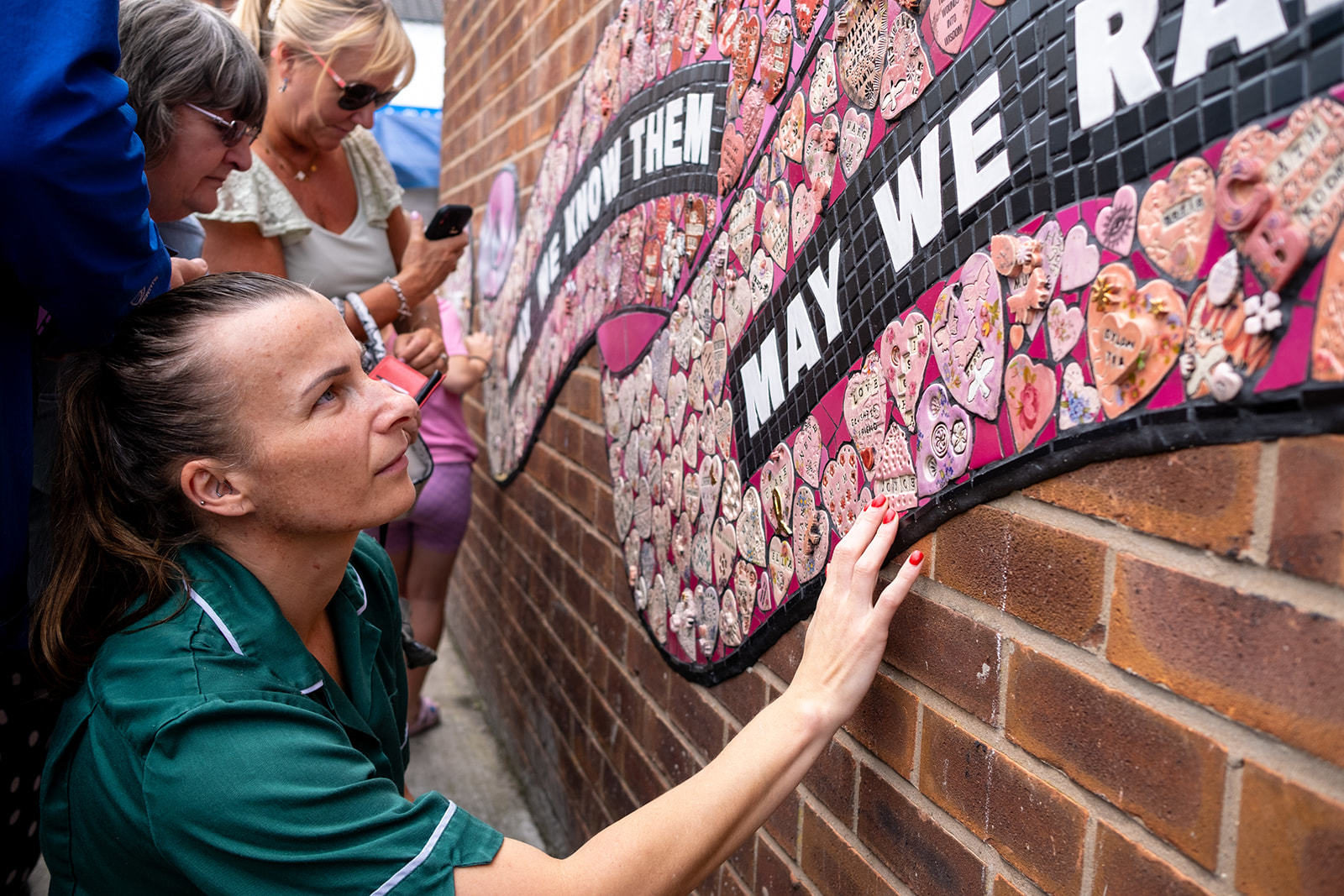 A woman in a nurse's uniform looks up close at the mosaic with one hand on it, her expression is thoughtful.