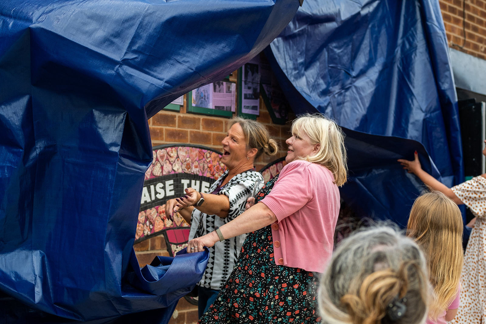 Carrie and a member of the St Helens community tear away the dark blue tarpaulin to reveal the mural.
