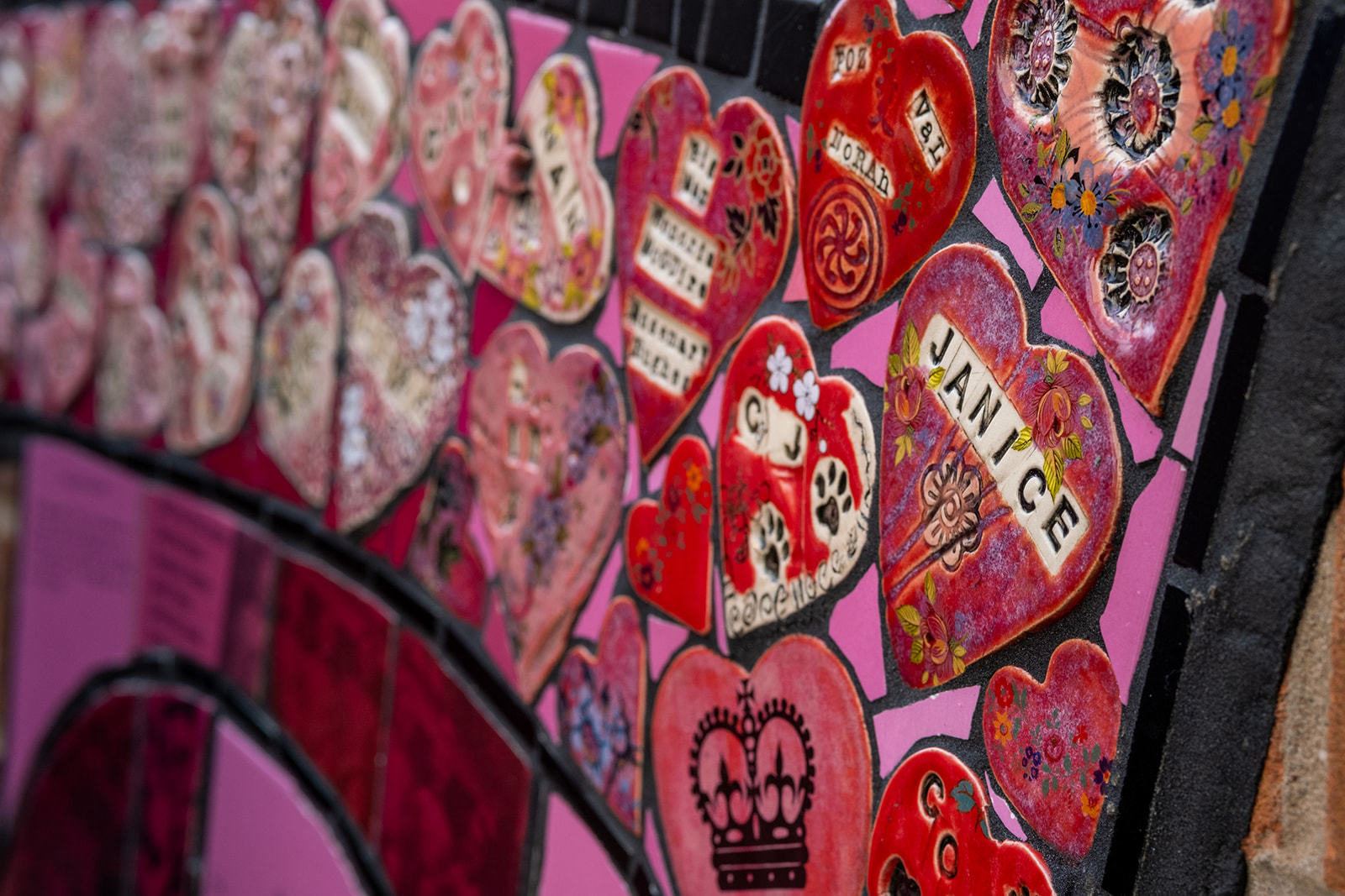 A close up photograph of the Strong Women of St Helens mural, there are clay hearts in different shades of red and dark pink that read 'Janice', 'CJ', and 'Foz, Val, Nora'.