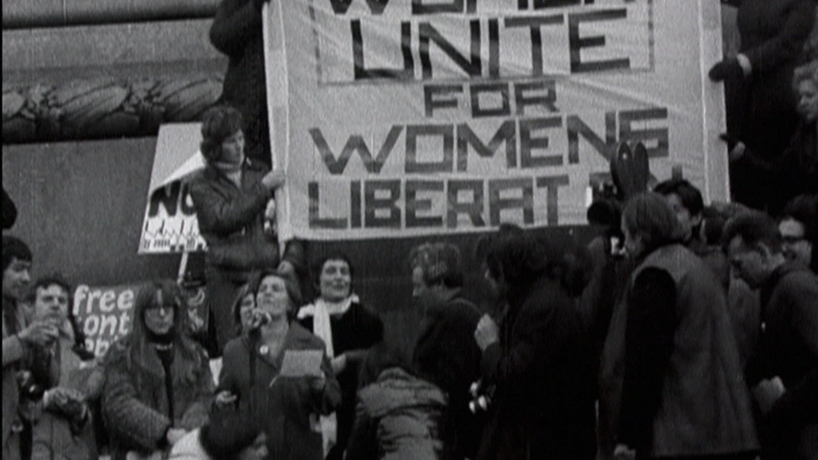 Black and white image of a protest. A group of women hold a banner which reads 'Women Unite for Women's Liberty'