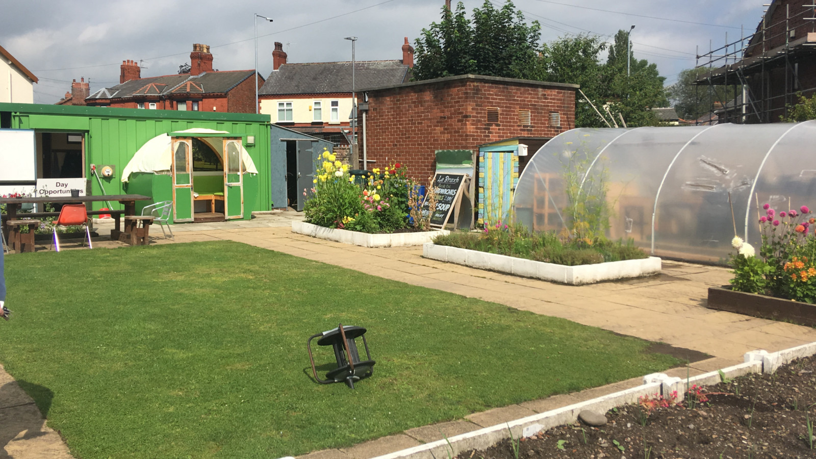 A garden with a patch of grass, a large green shed and a polytunnel.