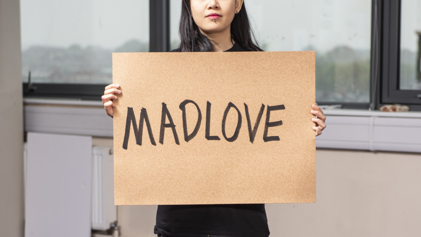 Artist Hannah Madness holding up a sign that reads 'MADLOVE' written in black marker, all caps.