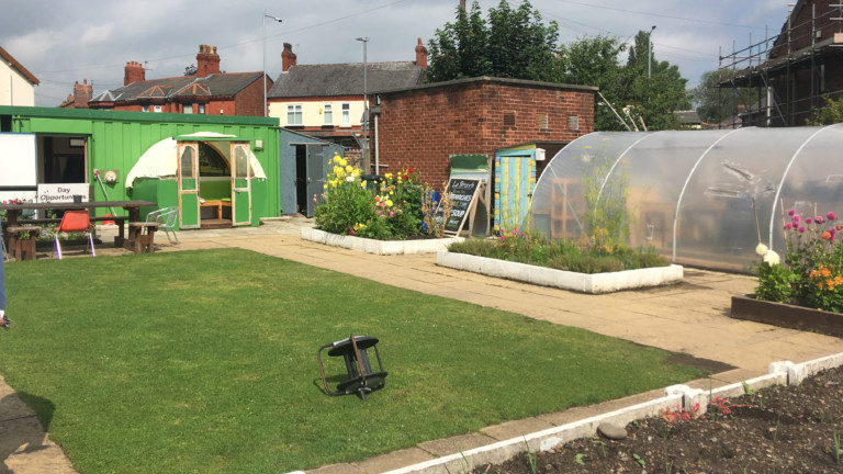 A garden with a patch of grass, a large green shed and a polytunnel.