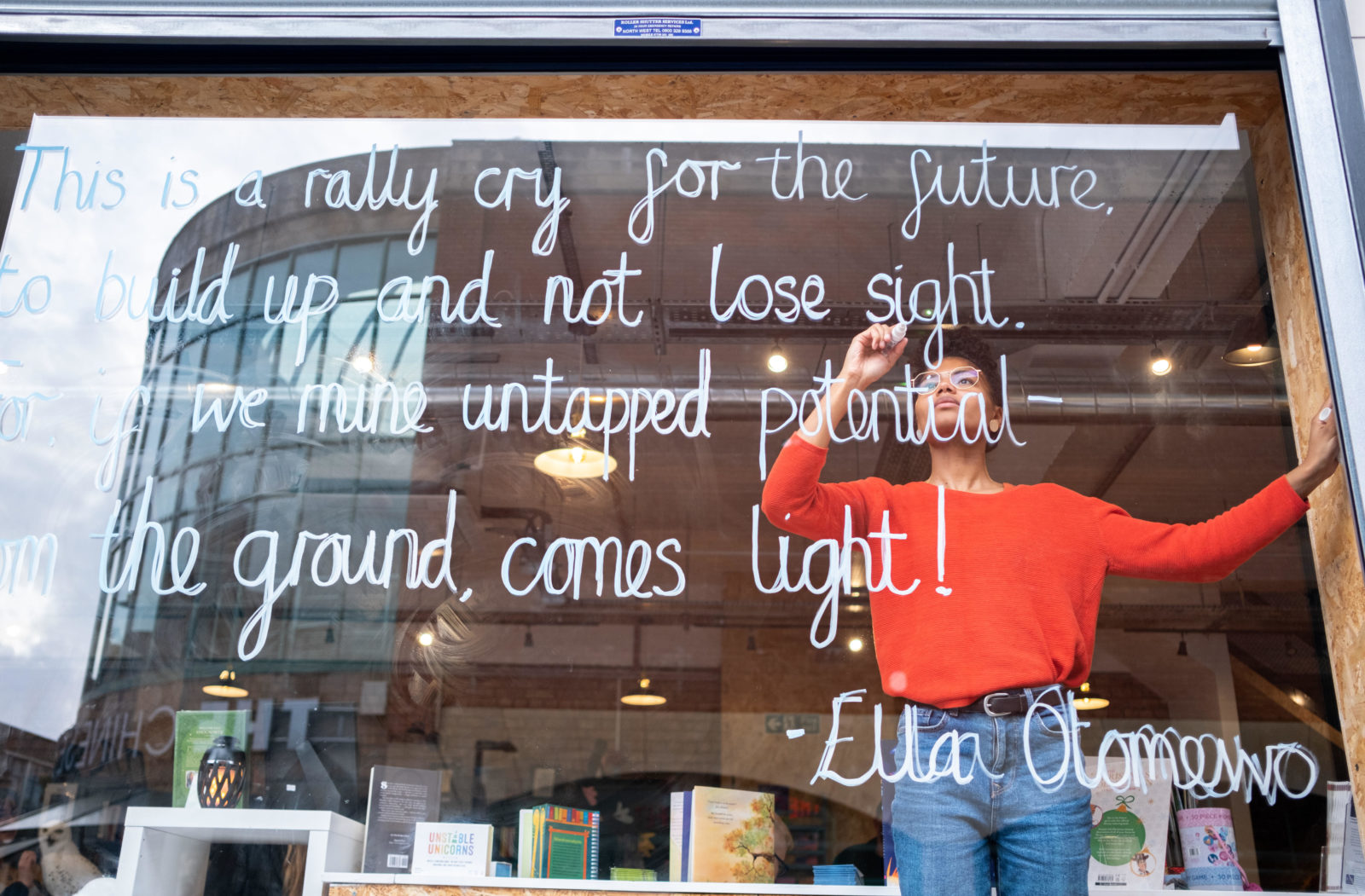 Ella inside The Book Stop writing poem on the window