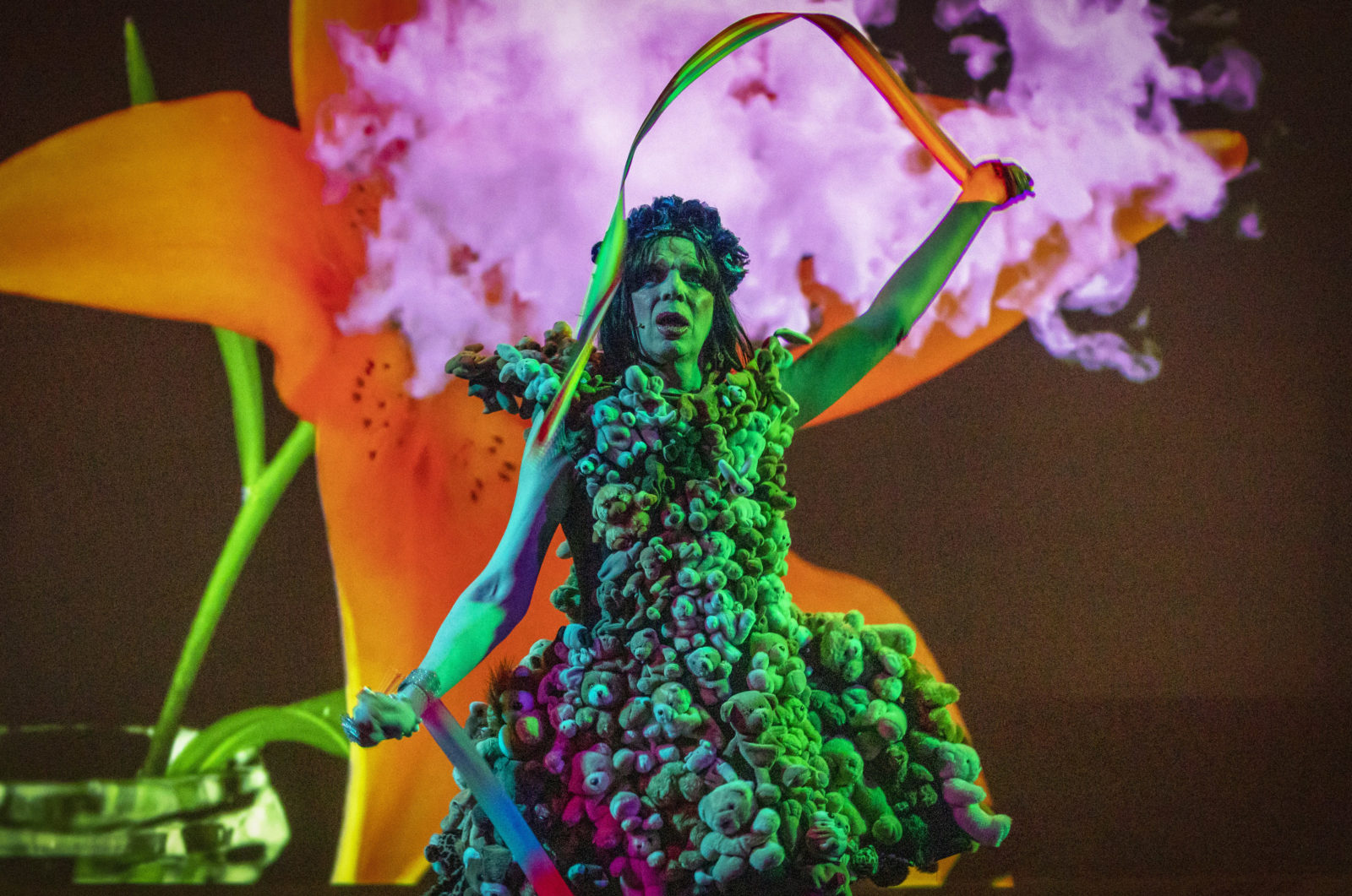 David Hoyle wearing a dress made of teddy bears, with pink smoke in the background.