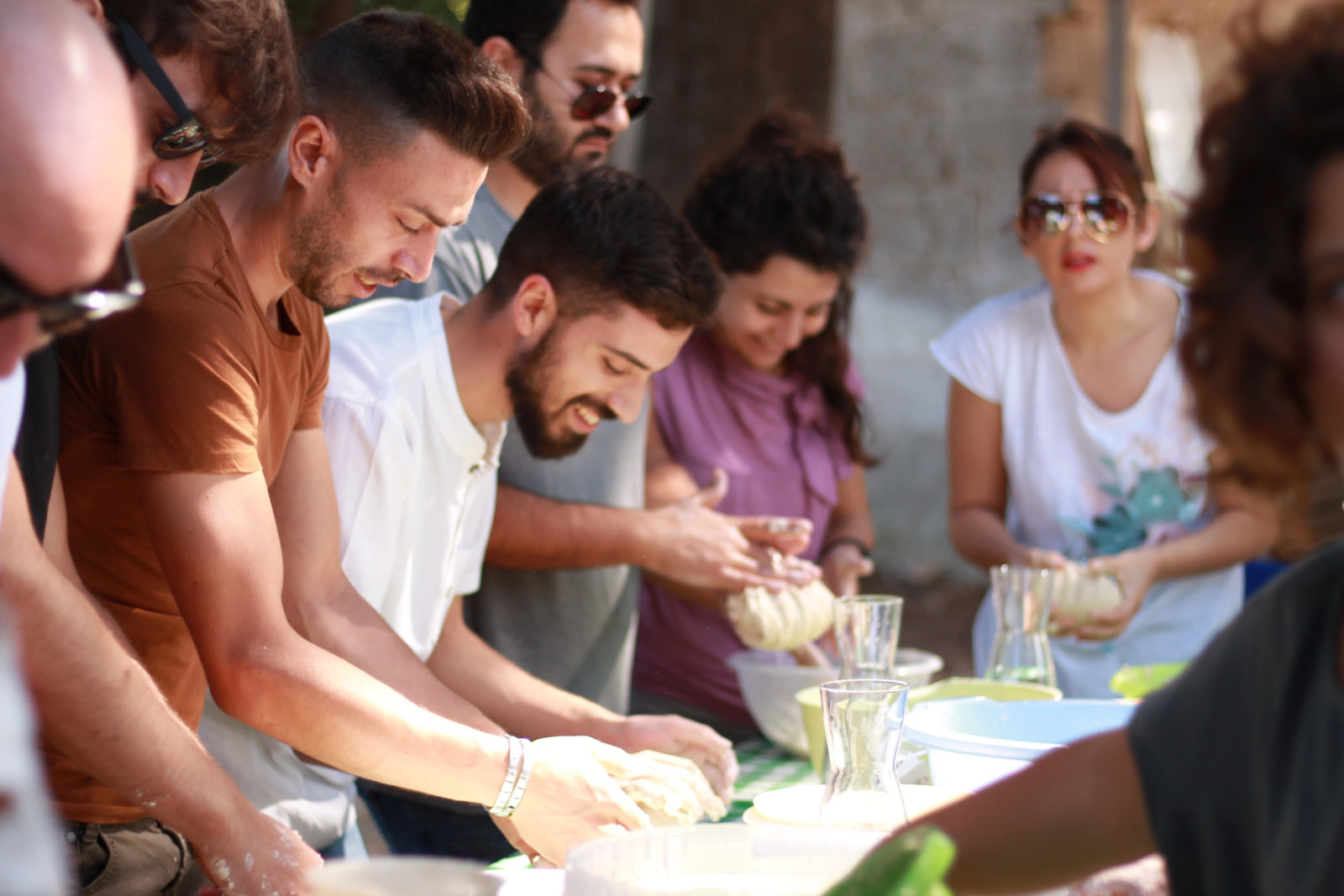 A group of people are standing around a table they are kneading dough and smiling