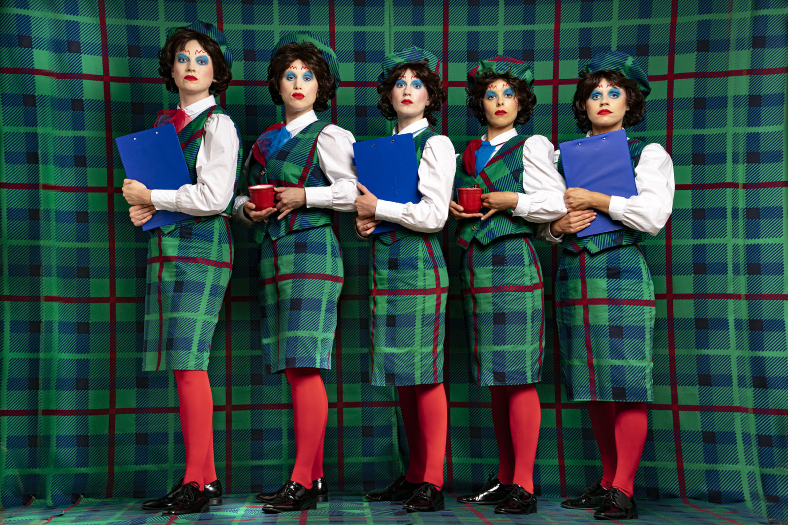 The artists dressed in tartan on a tartan background, with dramatic make up and stern facial expressions.