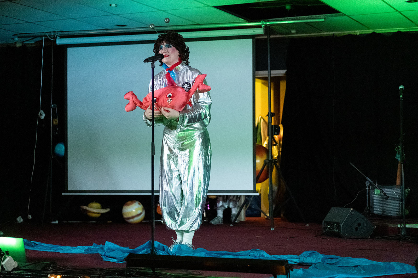 Member of figs in wigs holding up toy crab on stage