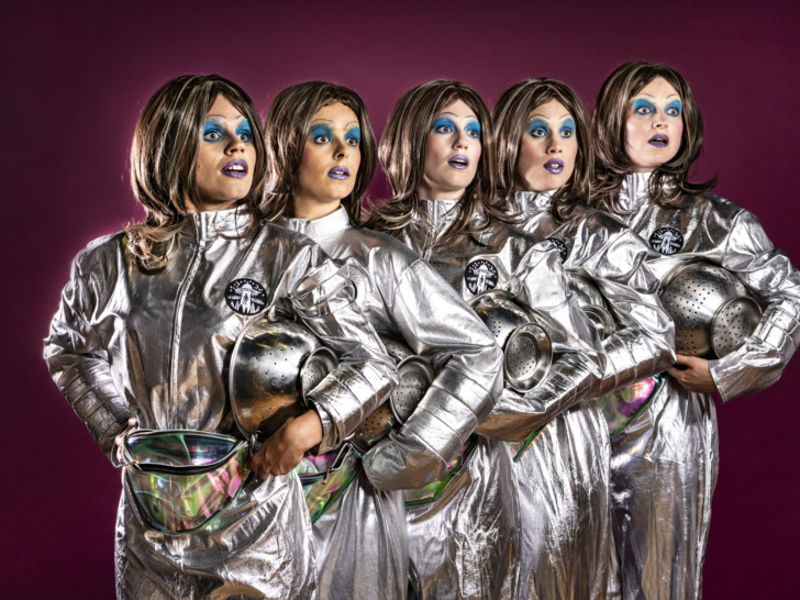 The artists dressed as astronauts in silver suits, with raised eyebrows and dramatic blue eyeshadow.