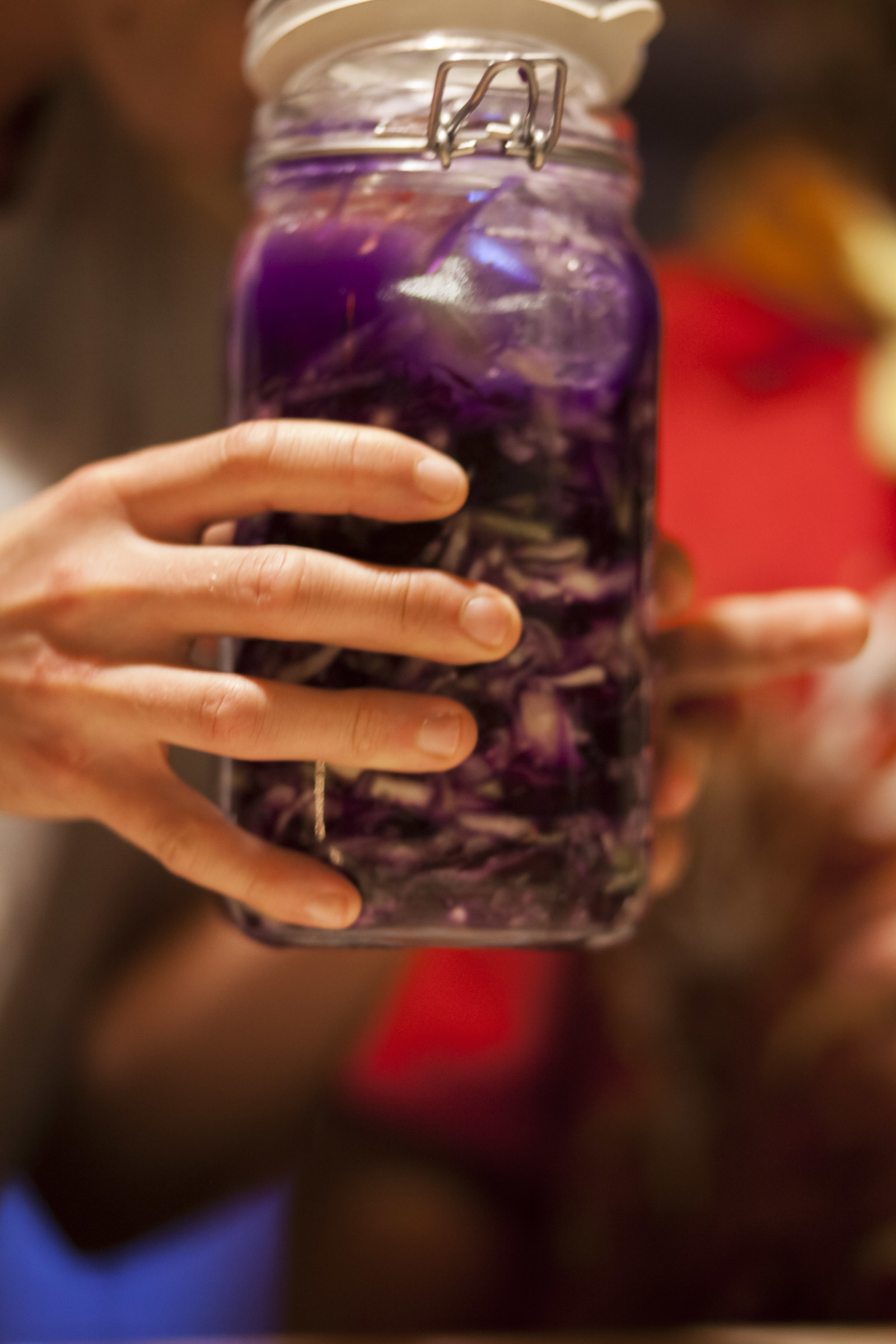 A pair of hands holding a jar of red cabbage sauerkraut.