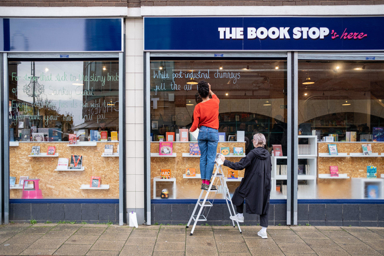 Ella writing poem on the outside of the window at The Book Stop on a ladder.