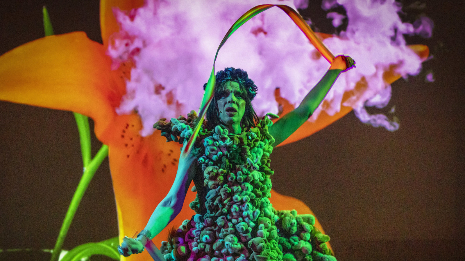 David Hoyle wearing a dress made of teddy bears, with pink smoke in the background.