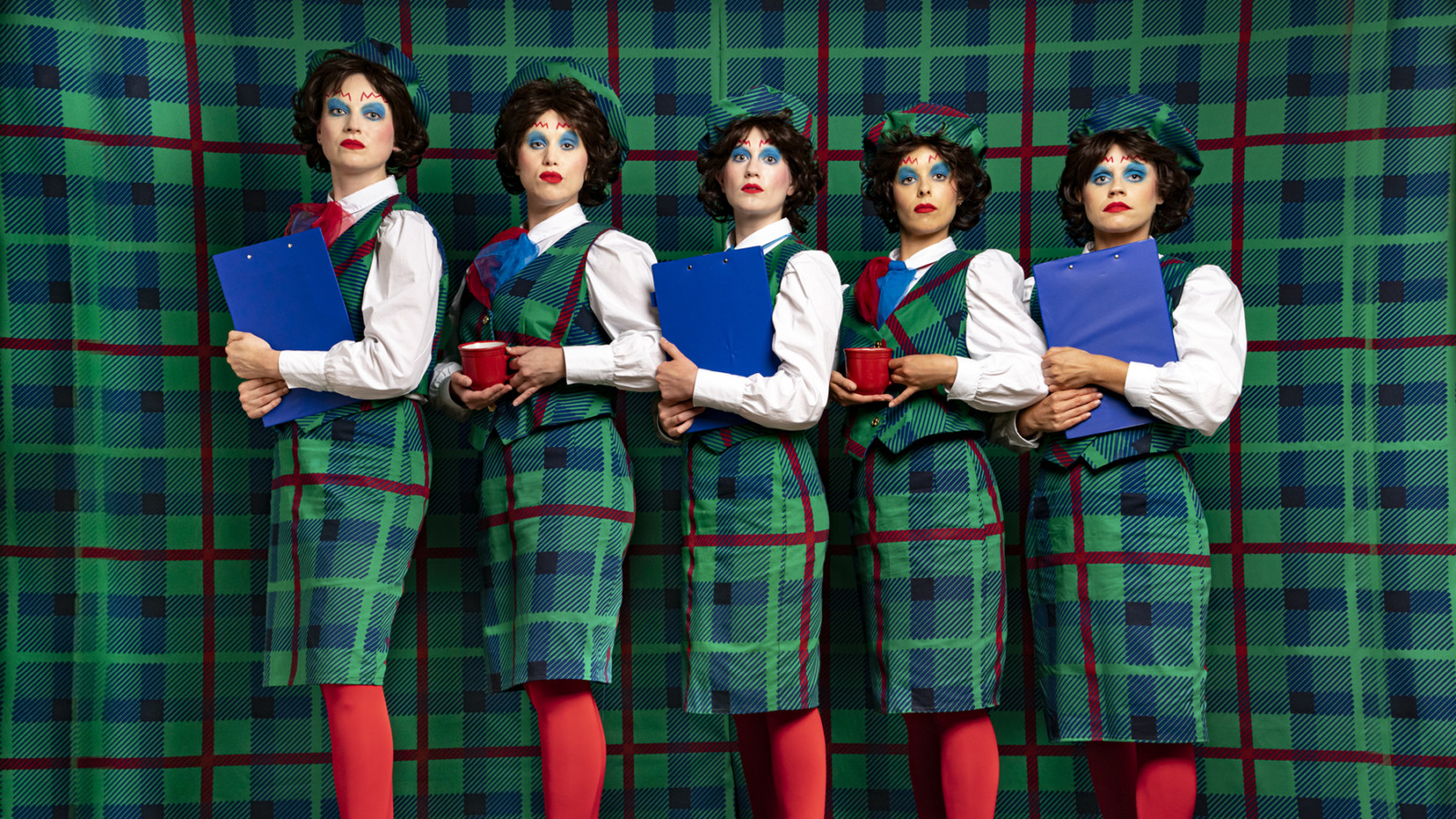 The artists dressed in tartan on a tartan background, with dramatic make up and stern facial expressions.