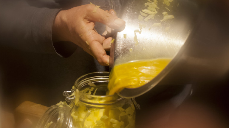 An abstracted image of sauerkraut being poured from a metal bowl into a glass jar.