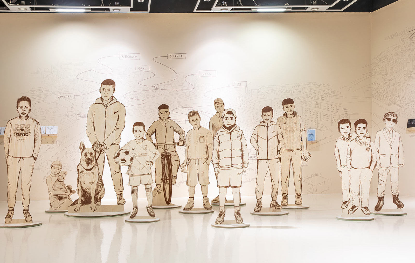 A collection of illustrated boys printed as large cut outs and arranged in a 3D display with a hand drawn illustrated map back drop of the same style.