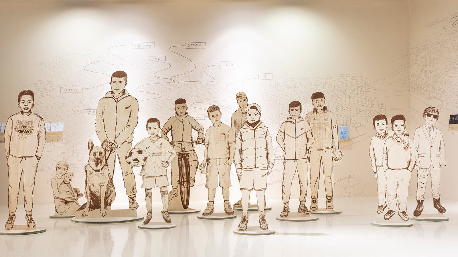 A collection of illustrated boys printed as large cut outs and arranged in a 3D display with a hand drawn illustrated map back drop of the same style.