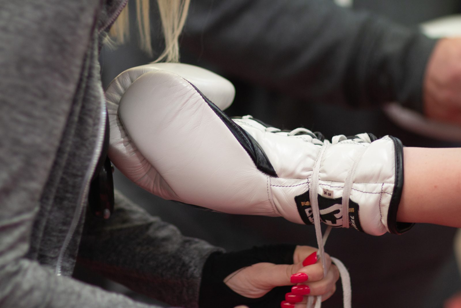 A person with bright red nails ties the laces on a white boxing glove.