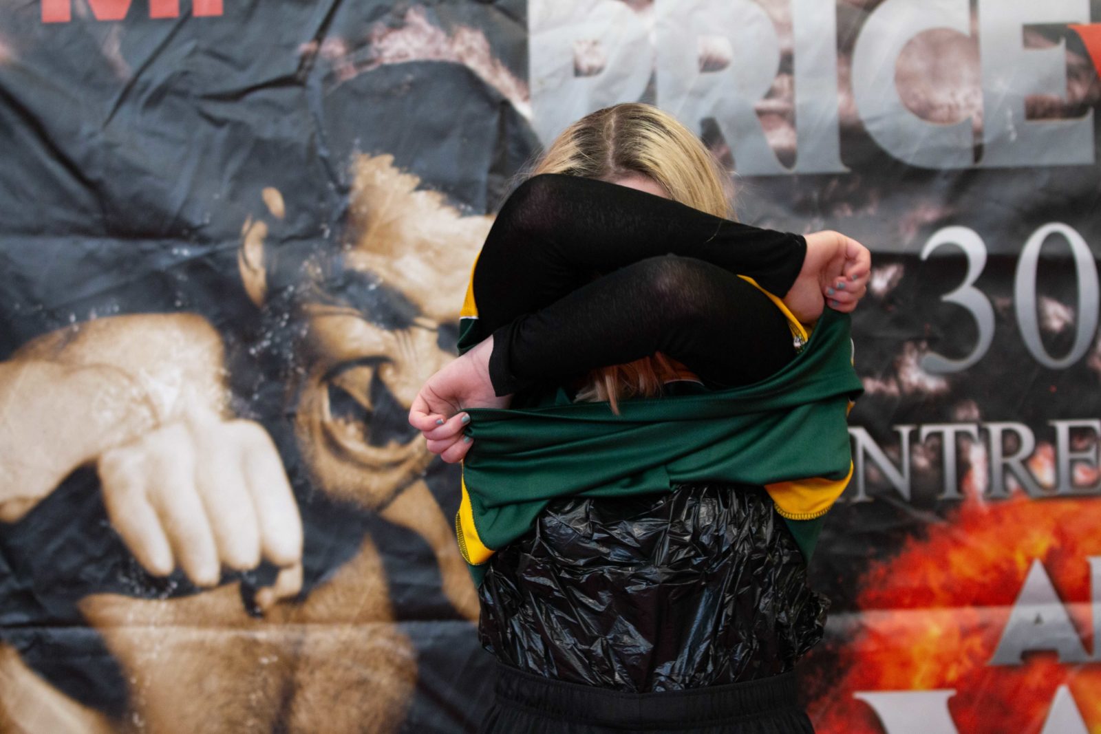 A person is removing a green and yellow sports top. They have a black long sleeved top underneath.