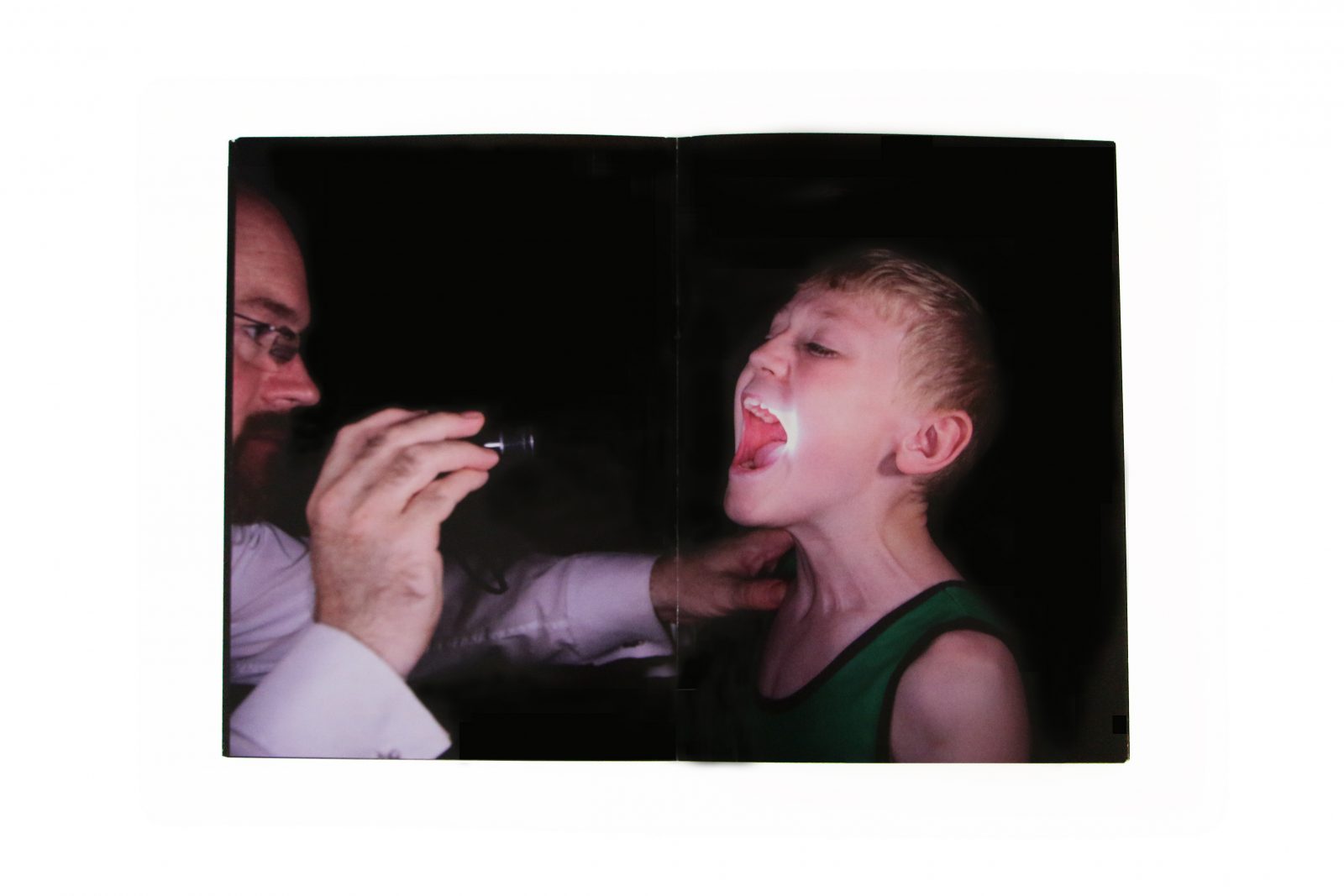 A man points a torch in to a young persons mouth.