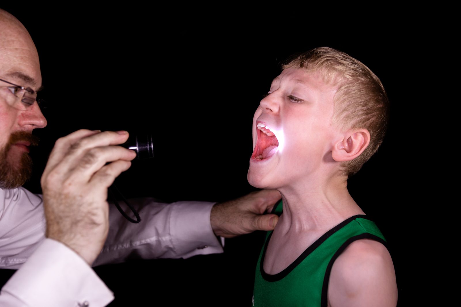 A man points a torch in to a young persons mouth.