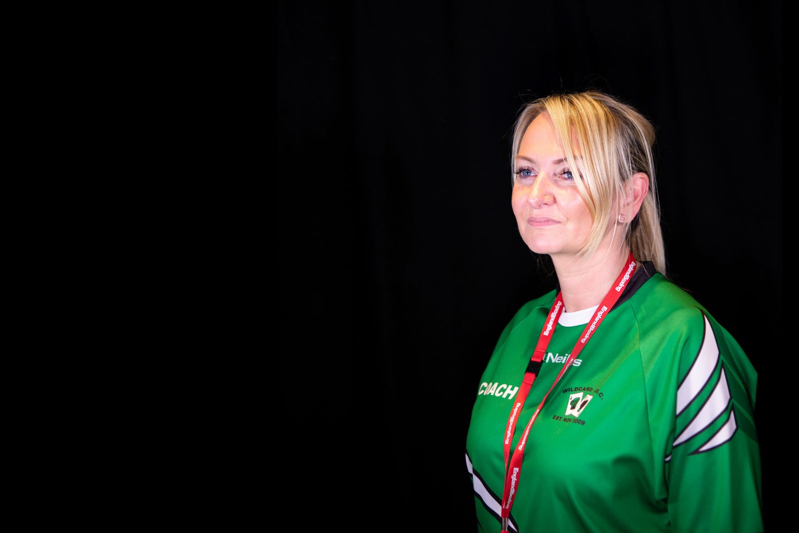 A woman in a green sports top and a red lanyard around her neck looks in to the distance and smiles.