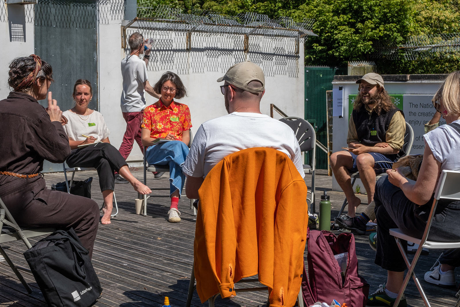 A group of people sit in a circle on chairs on a patio having a discussion, they are smiling and laughing.