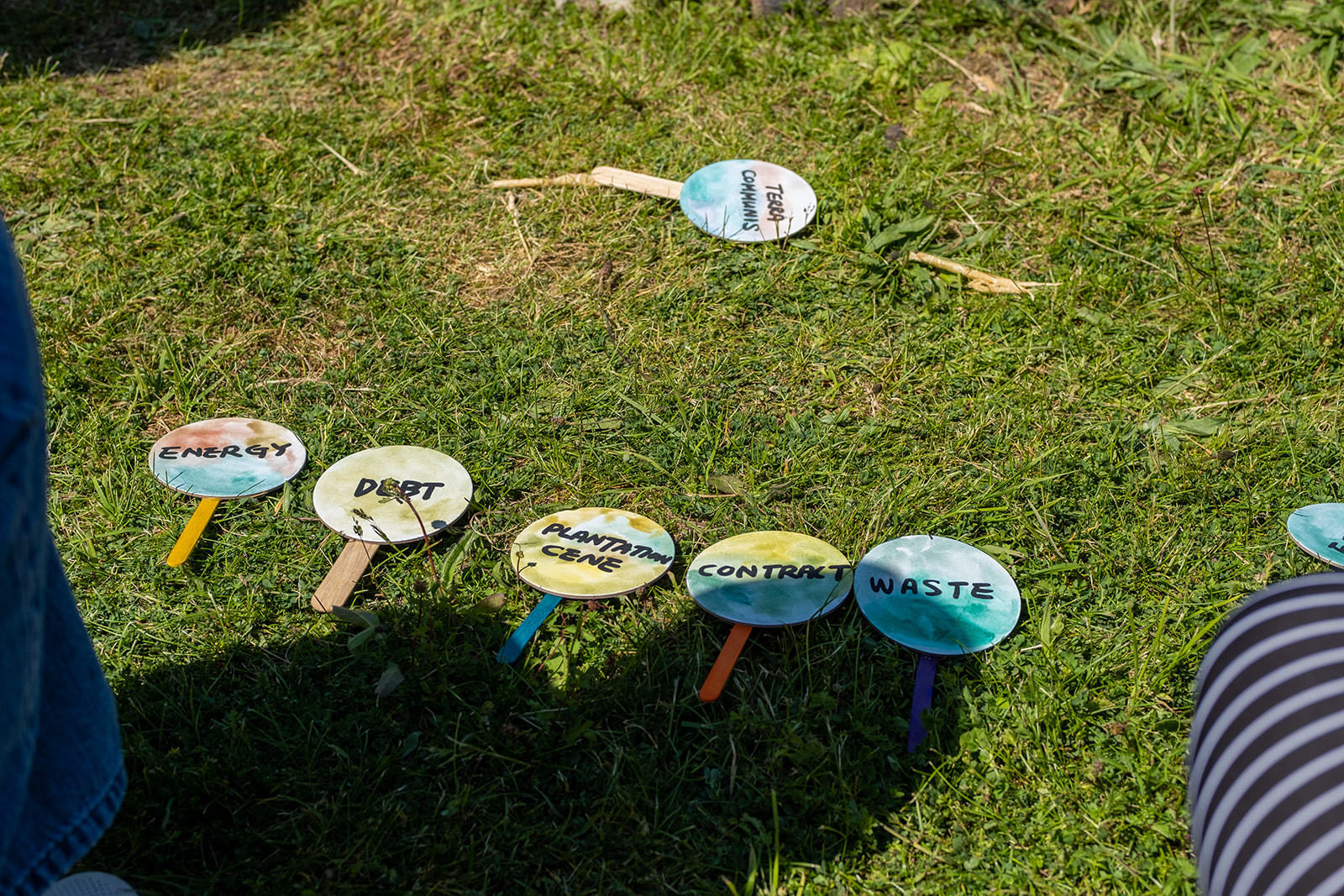 Mini signs are laid out on the grass that read 'Terra Communis', 'Energy', 'Debt', 'Plantation cane', 'Contract', and 'Waste'.