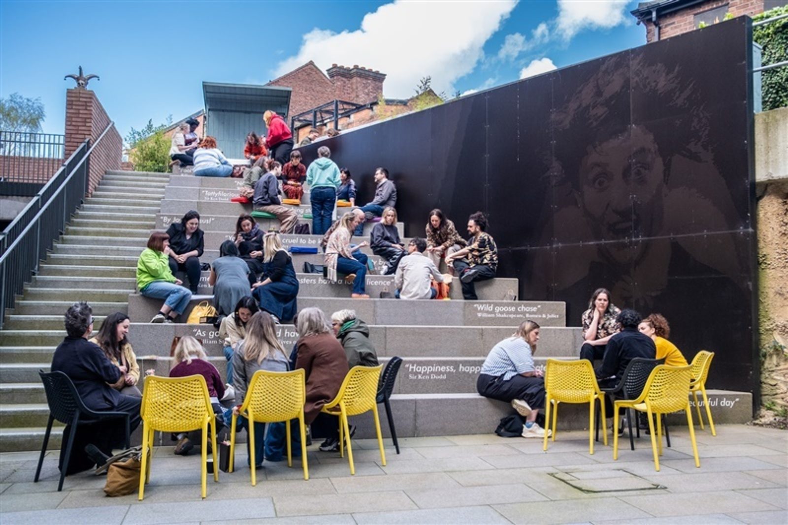 A number of people are gathered in small groups, sitting in discussion in their groups on a large set of concrete steps.