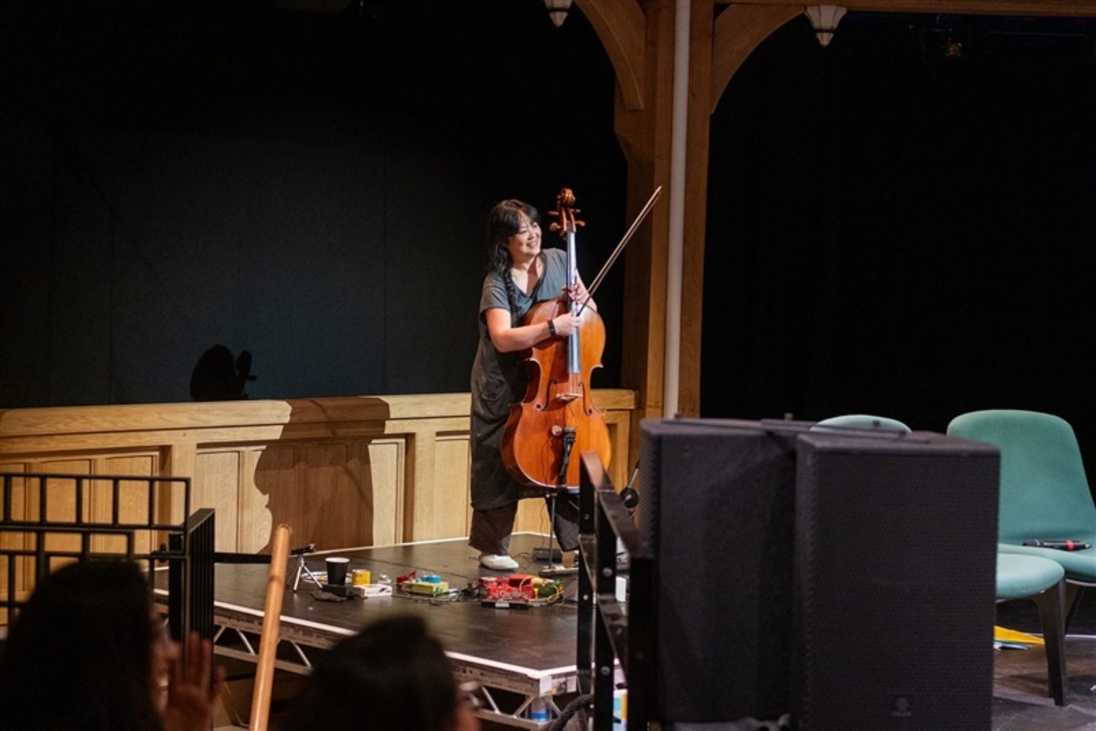 Semay Wu, stands on a stage playing cello and with a selection of musicians pedals at their feet.