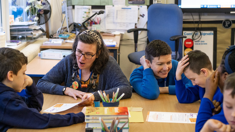 schoolkids in blue uniform sit around a table laughing whilst going through the schools resource with heart of glass producer Nat and Interference art's Maura.
