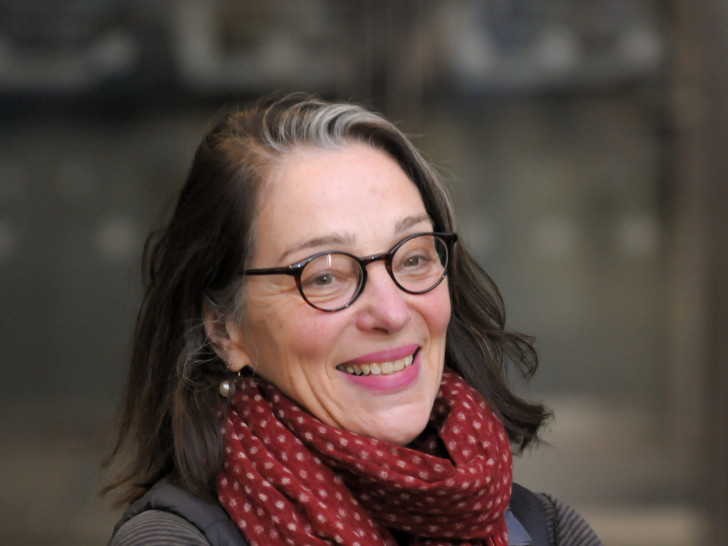 Julia is photographed smiling past the camera, she has dark hear and wears glasses and a red polka dot scarf around her neck.