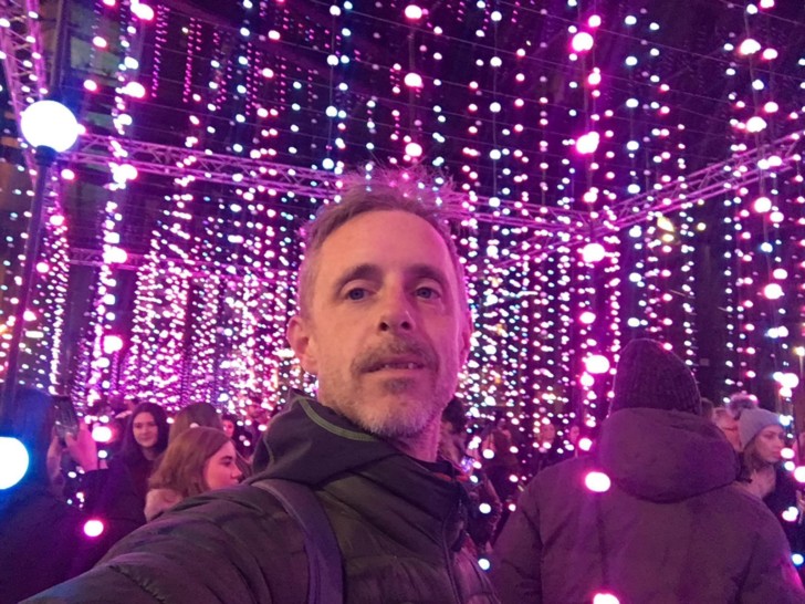 Richard is photographed in a light installation surrounded by small pink bulbs. He has short grey hair.