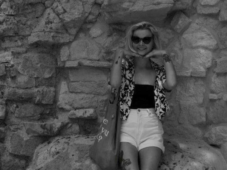 Black and white photo of Sinéad from Heart of Glass, smiling in front of a stone wall.