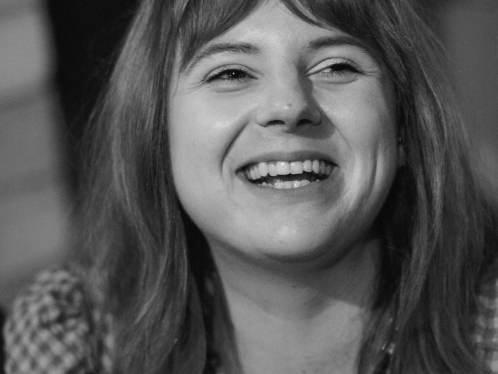 Black and white photograph of a smiling young woman with long dark hair and a fringe, wearing a gingham shirt.