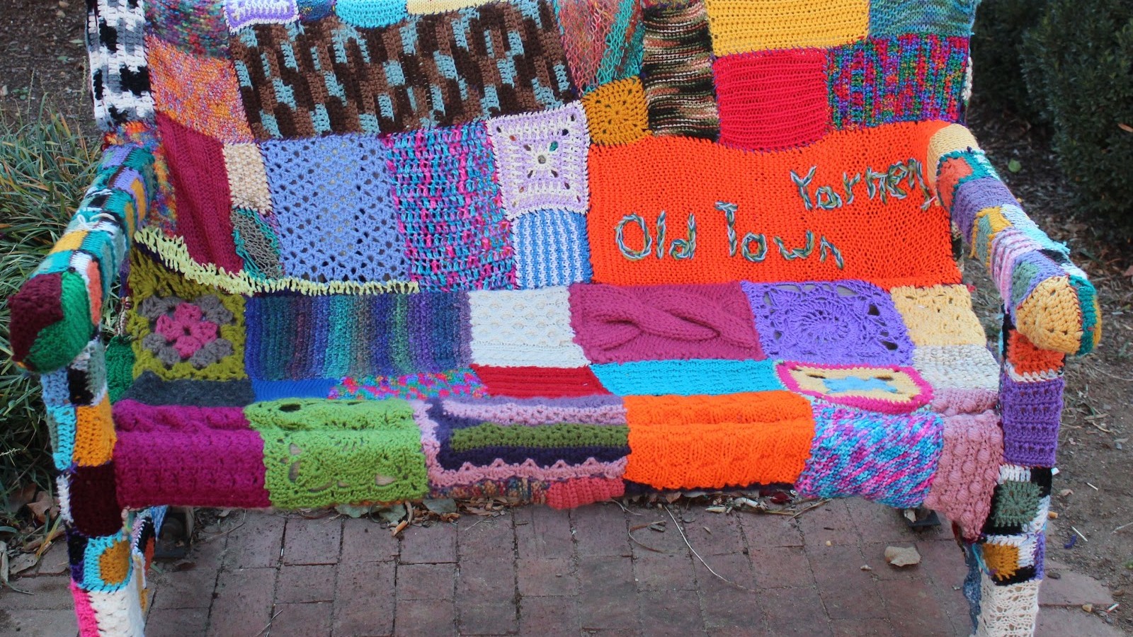 A bench is covered in a patchwork of bright and colourful knitting.