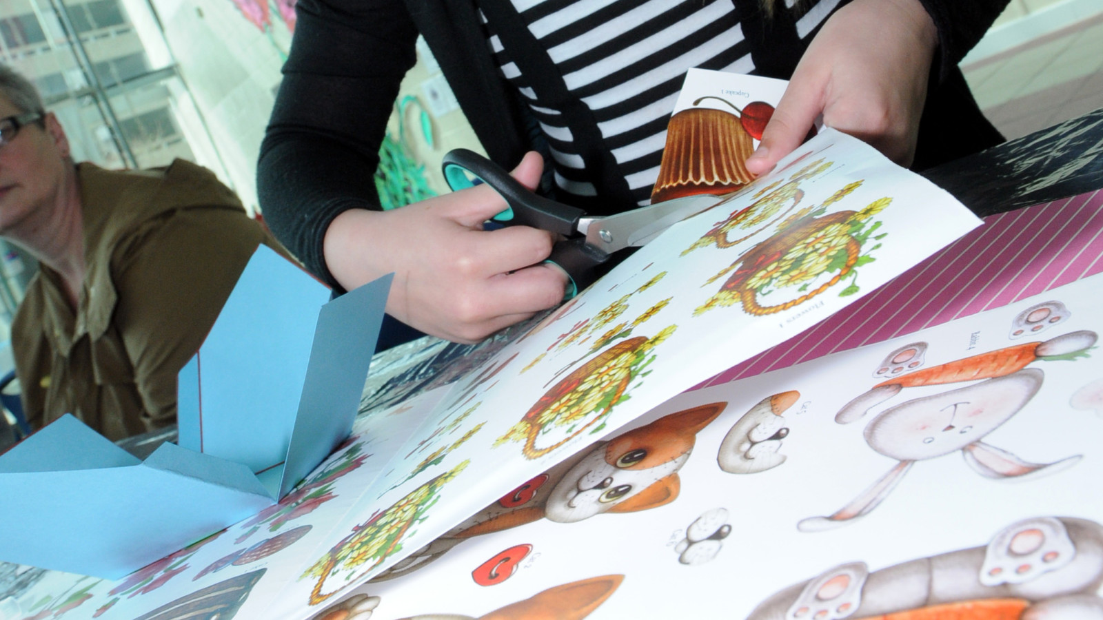 A young person is cutting out cartoon drawings of rabbits and dogs from pieces of white card.