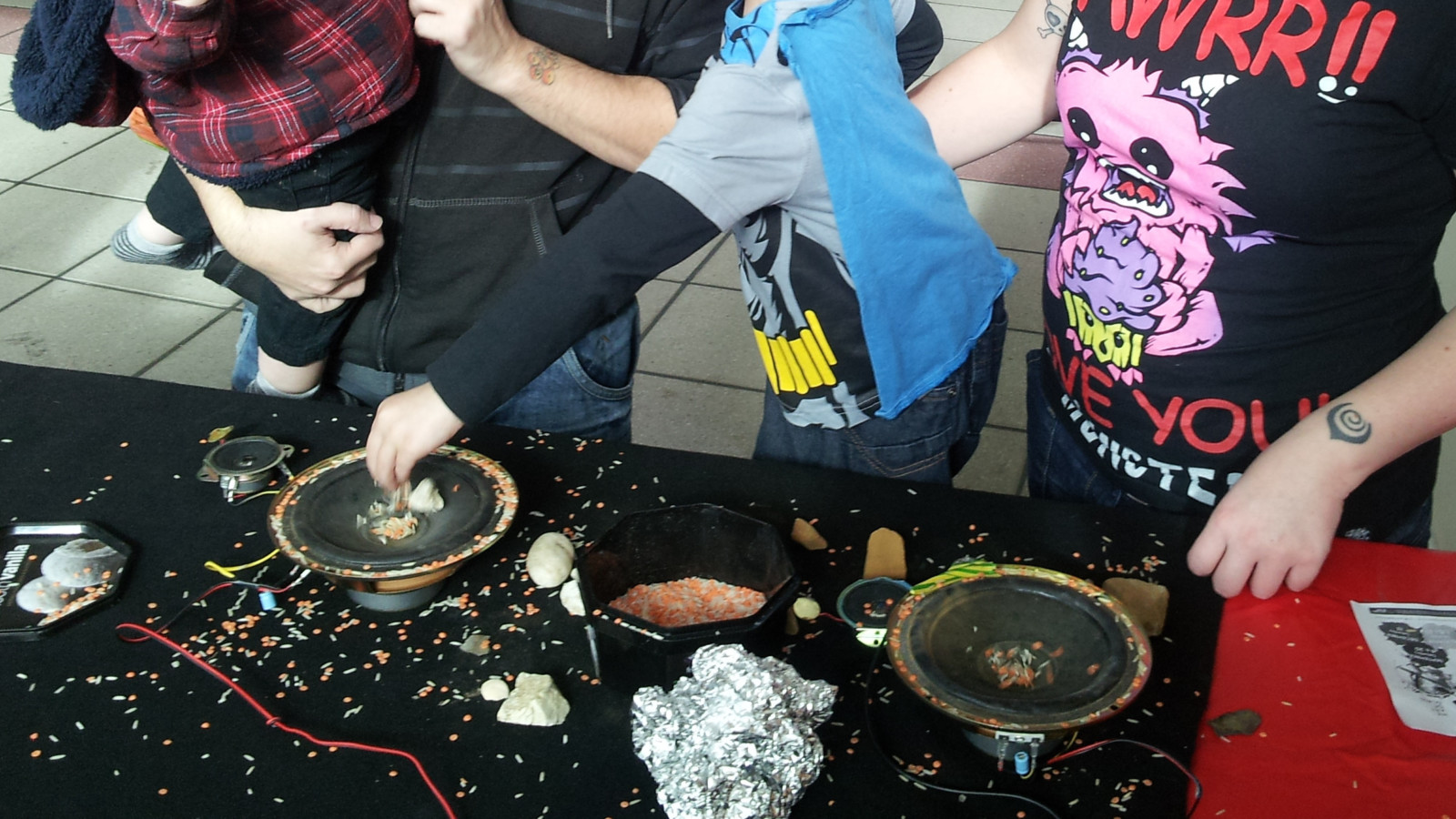 Two adults, with two children are placing colourful rice and foil on to a speaker cone.
