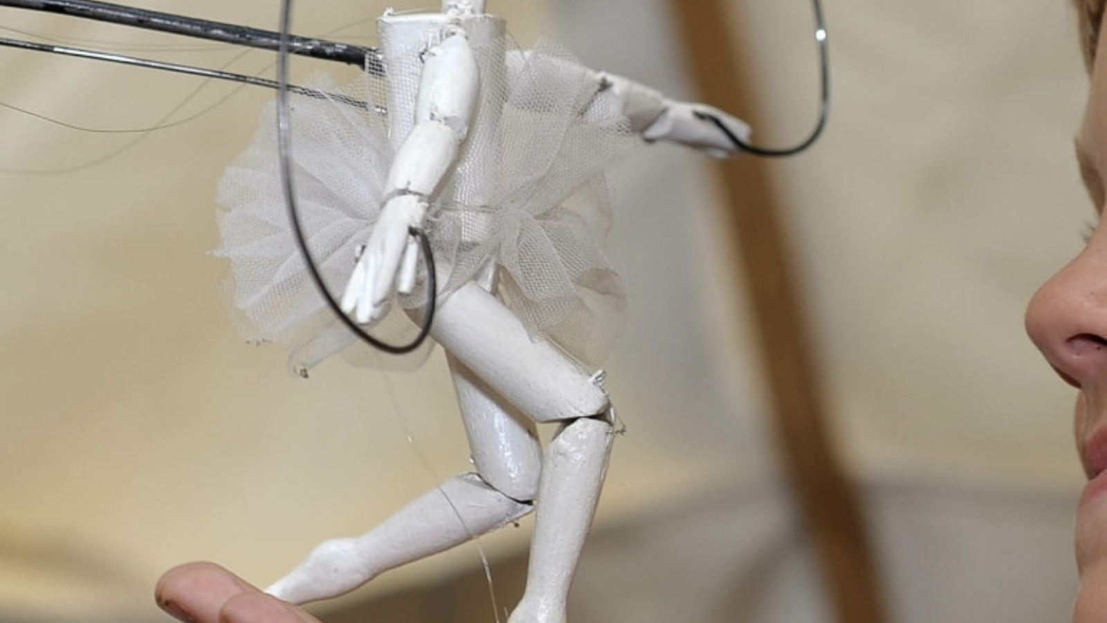 A small, white wooden drawing mannequin wearing a white tutu is posed on a persons hand.