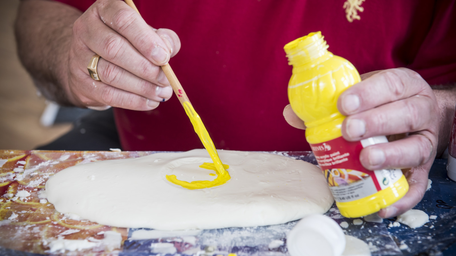 A person in a red t-shirt is painting a yellow circle on white dough.