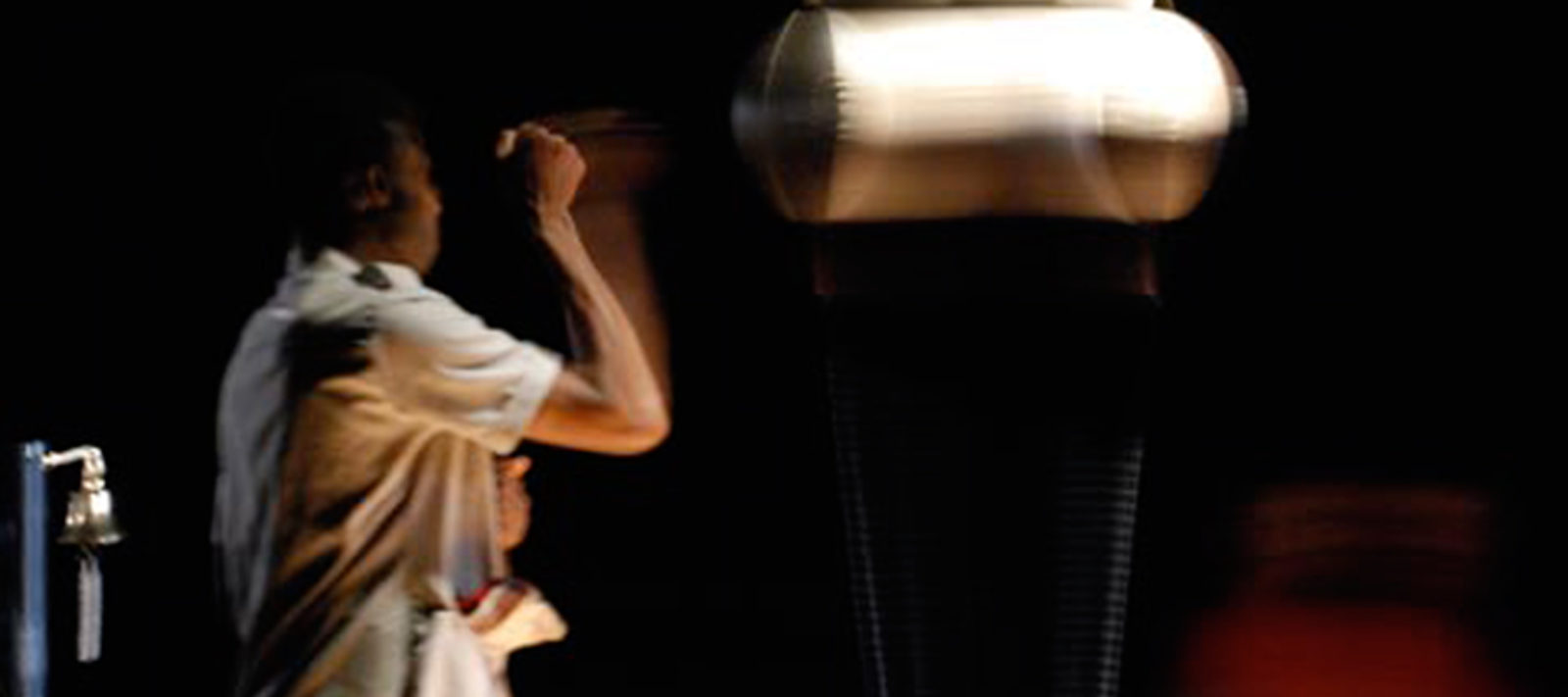 A person wearing a light coloured shirt stands in a dark room punching a punching bag.