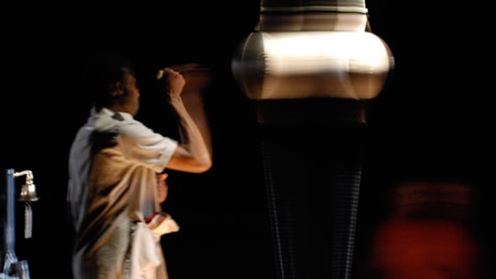 A person wearing a light coloured shirt stands in a dark room punching a punching bag.