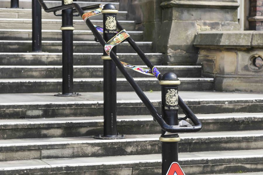 A large stone set of steps leads up to the front of a building. At the bottom of the stairs, attached to the handrail is a red triangular sign. There is also some tape wrapped around the handrails.