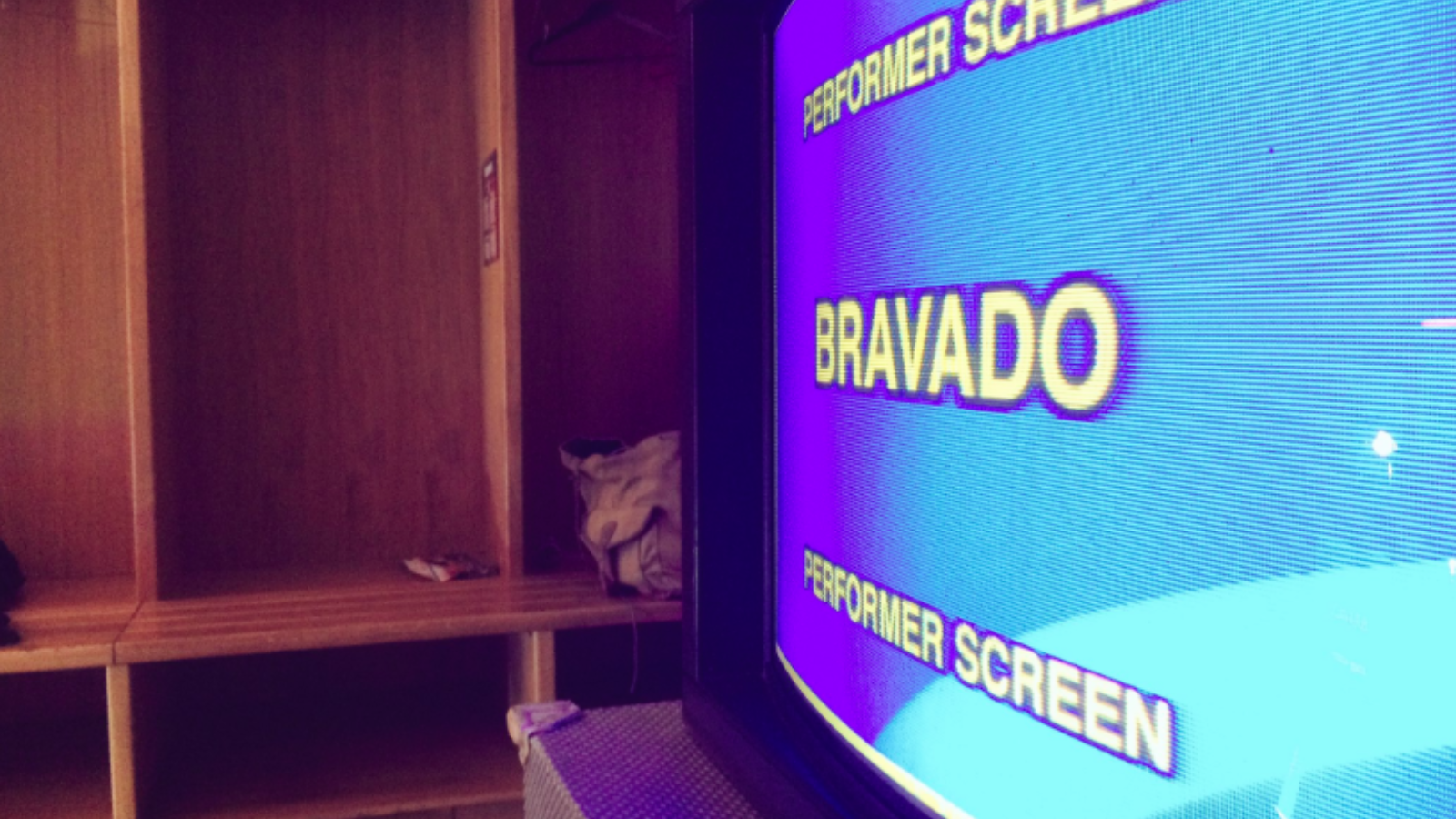 In a changing room a TV shows a bright blue screen showing the works 'Bravado' and 'Performer Screen' in white text.